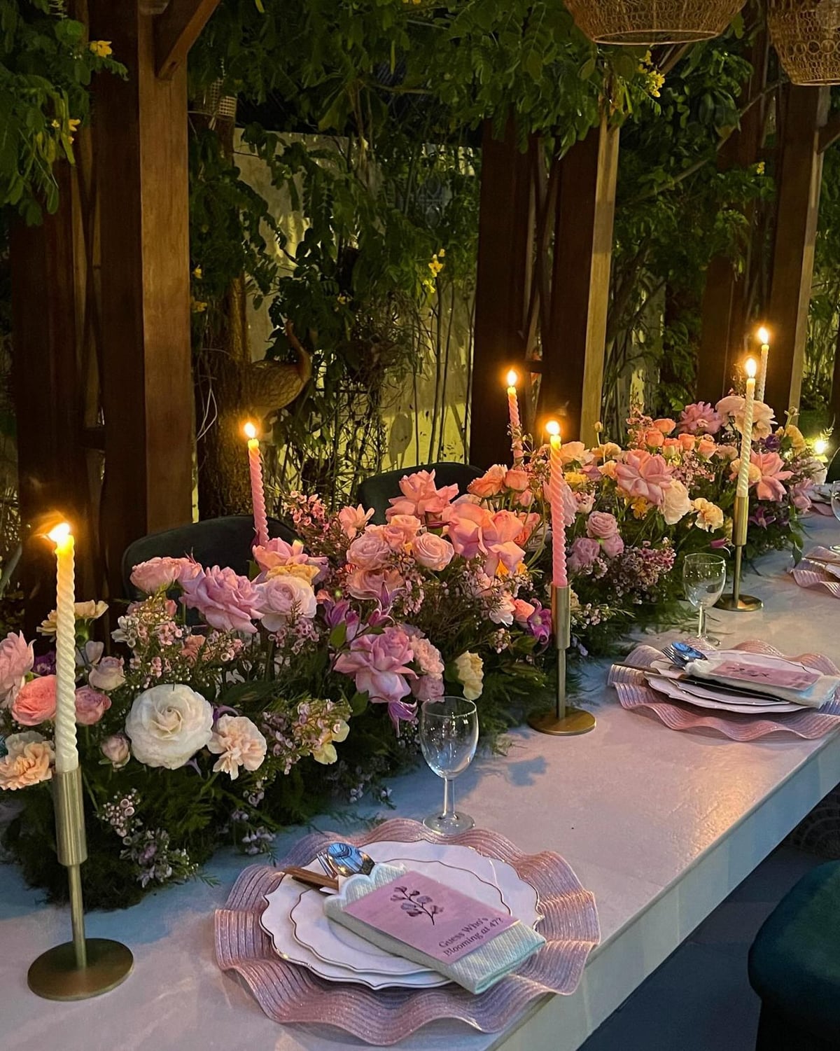 Pink and lilac floral arrangements with taper candles along a table set for an evening gathering.