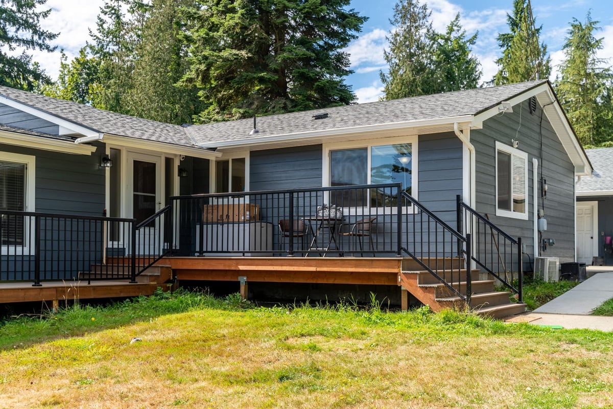 A newly remodeled home with a gray exterior, white trim, and a spacious wooden deck with black railings.