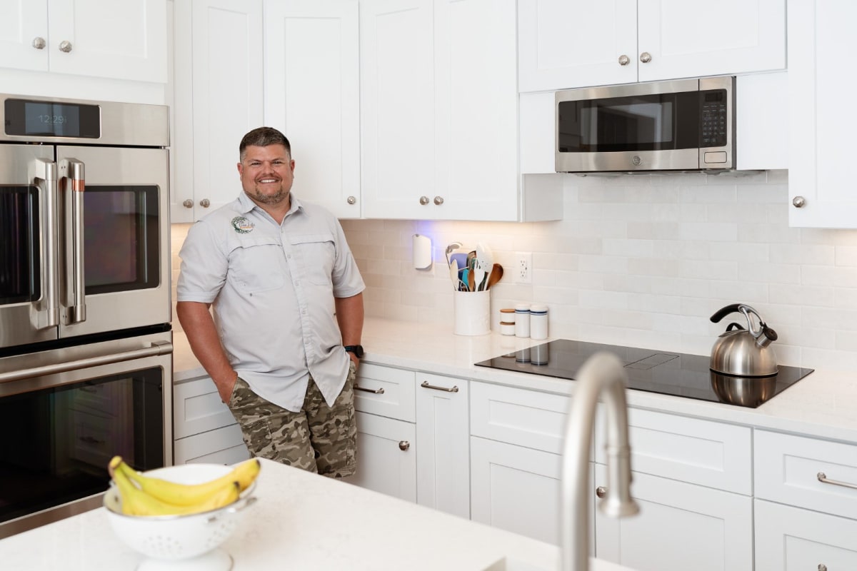 Jonathon Sprinkle standing in a bright, modern kitchen featuring white shaker cabinets.